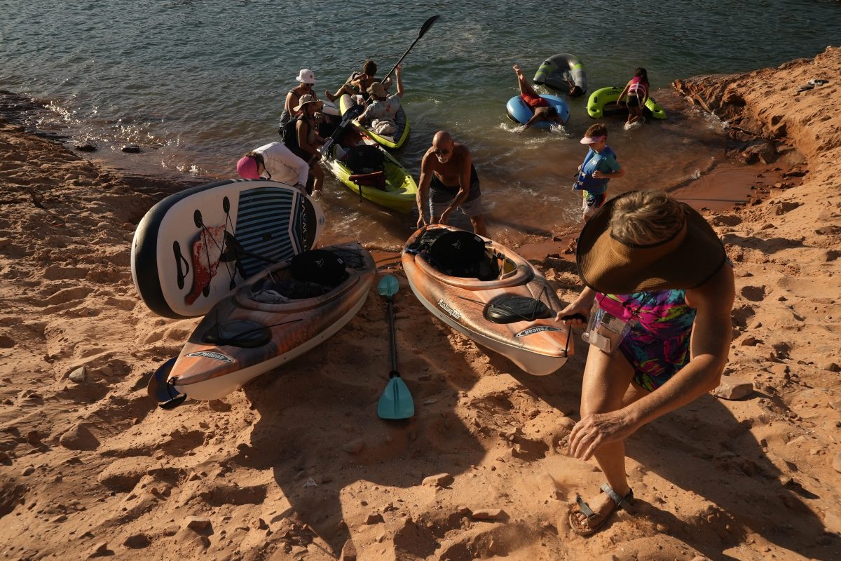 Tourists carry a kayak up a sandy hill Tuesday, June 7, 2022, in Page, Ariz.