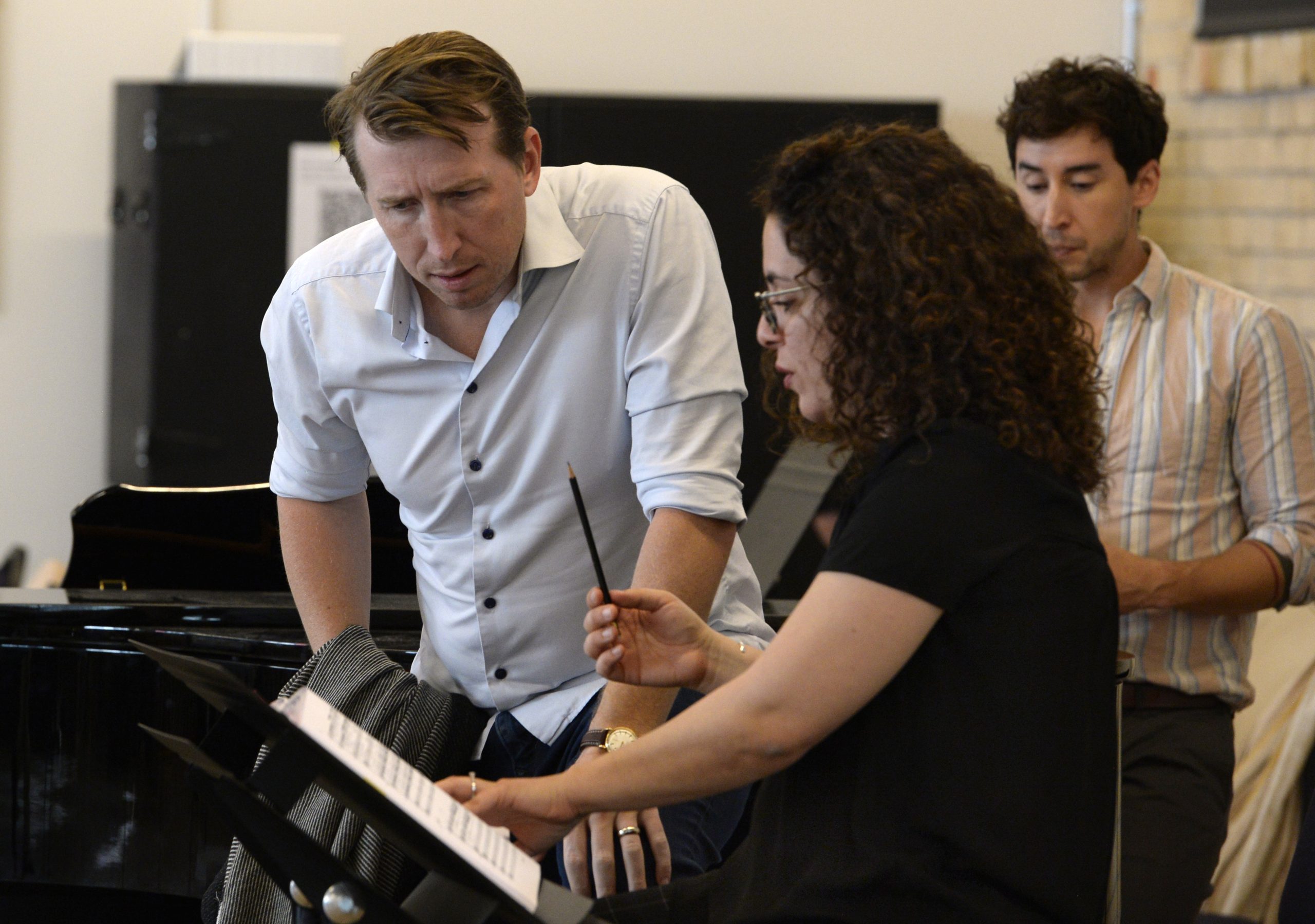 A man leans over to read sheet music as a woman points out a particular section.