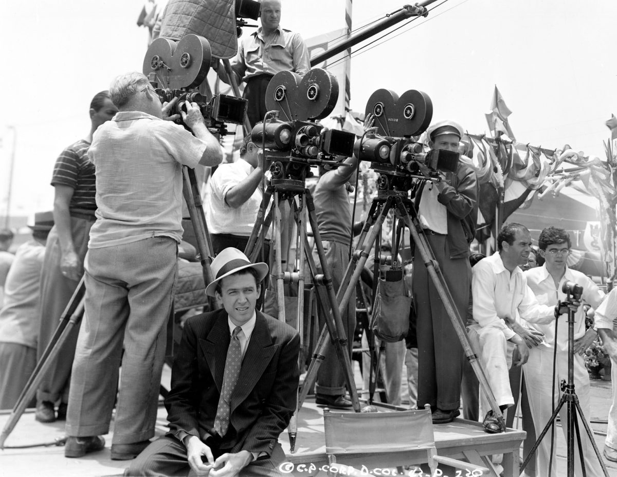 James Stewart sits down as a bunch of men work on cameras.