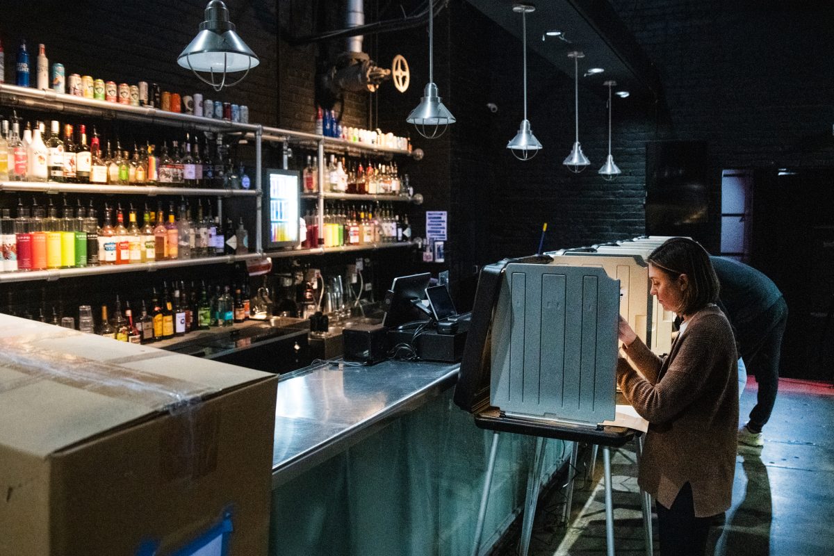 A woman fills out her ballot at a station set up in front of a bar.