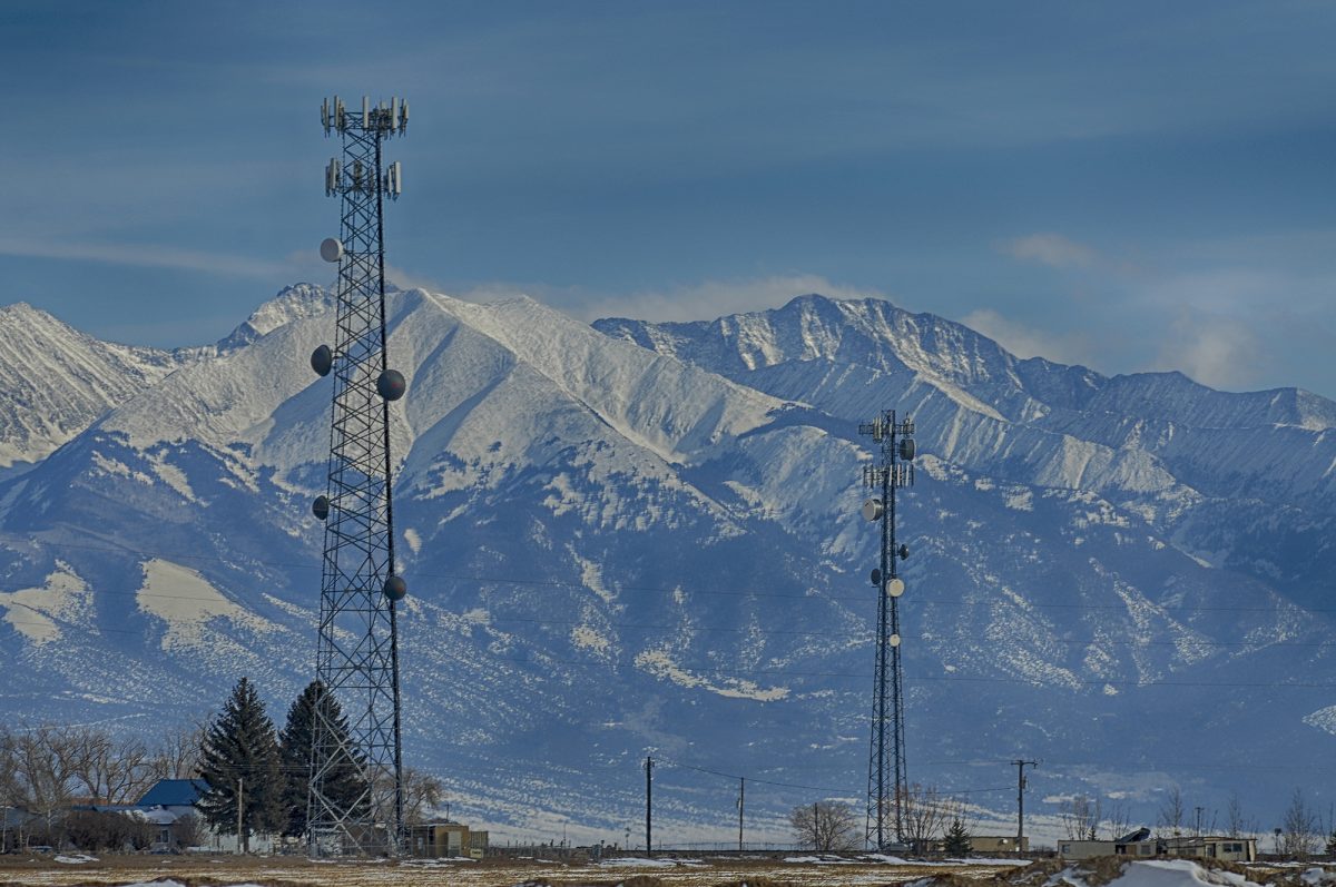 Two broadband towers stand in front of a mountain range.